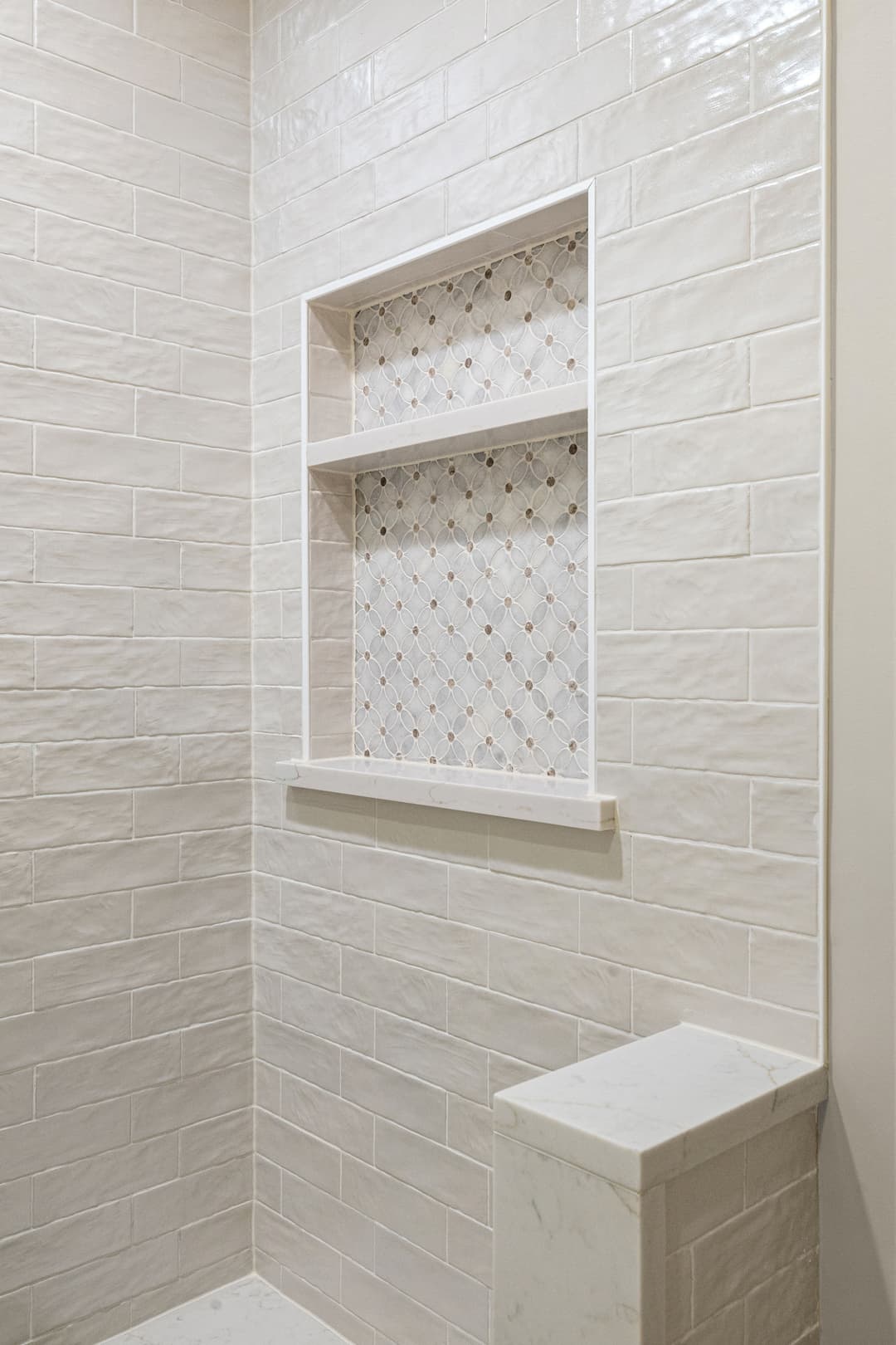 Modern bathroom shower with white tile, decorative niche, and stone accents. Bright and clean design.