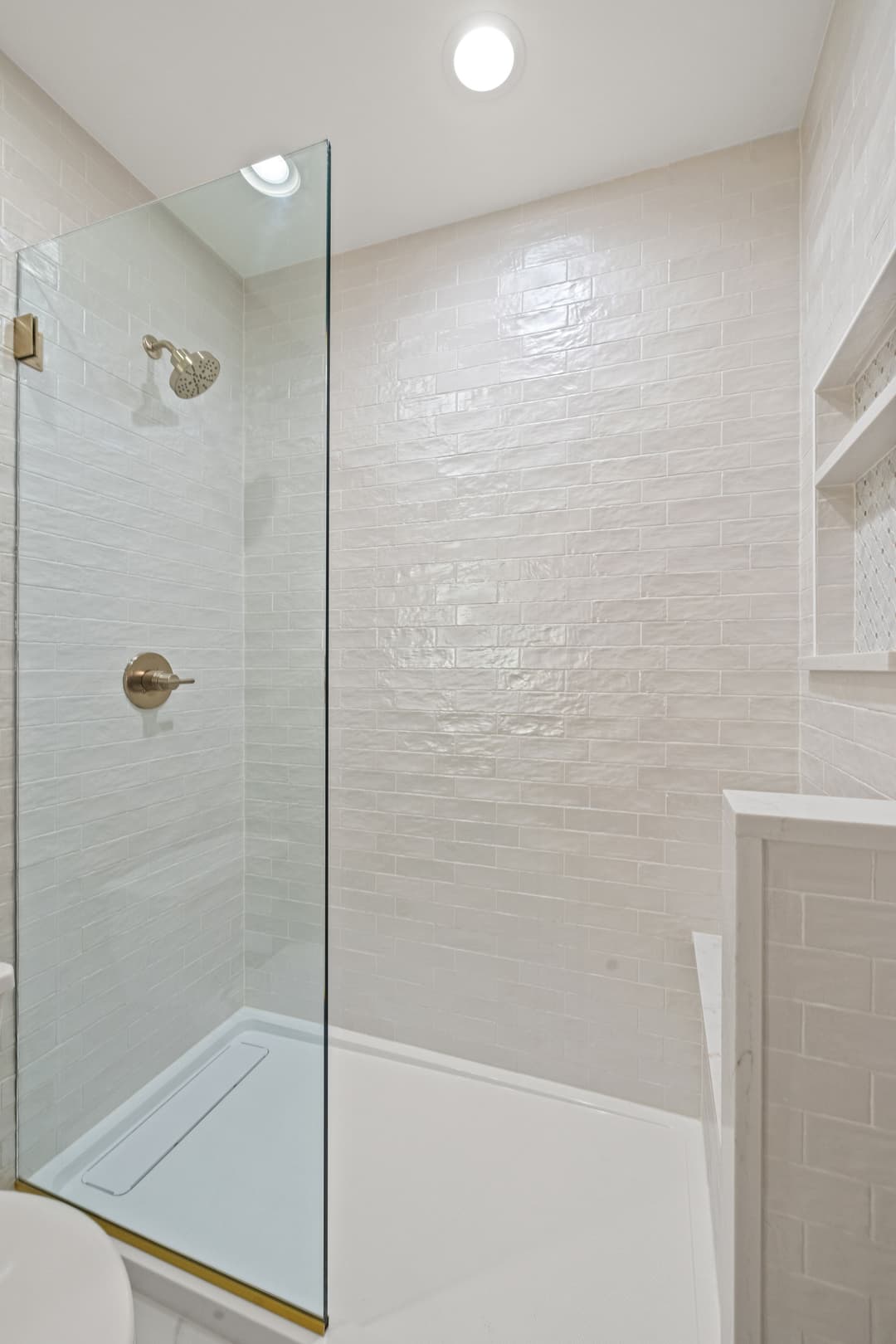 Modern glass shower enclosure with white tile walls and recessed shelves. Clean, minimalist design.