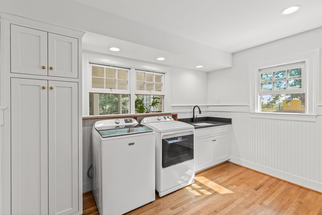 Modern laundry room featuring white washer and dryer, black countertops, and natural light.