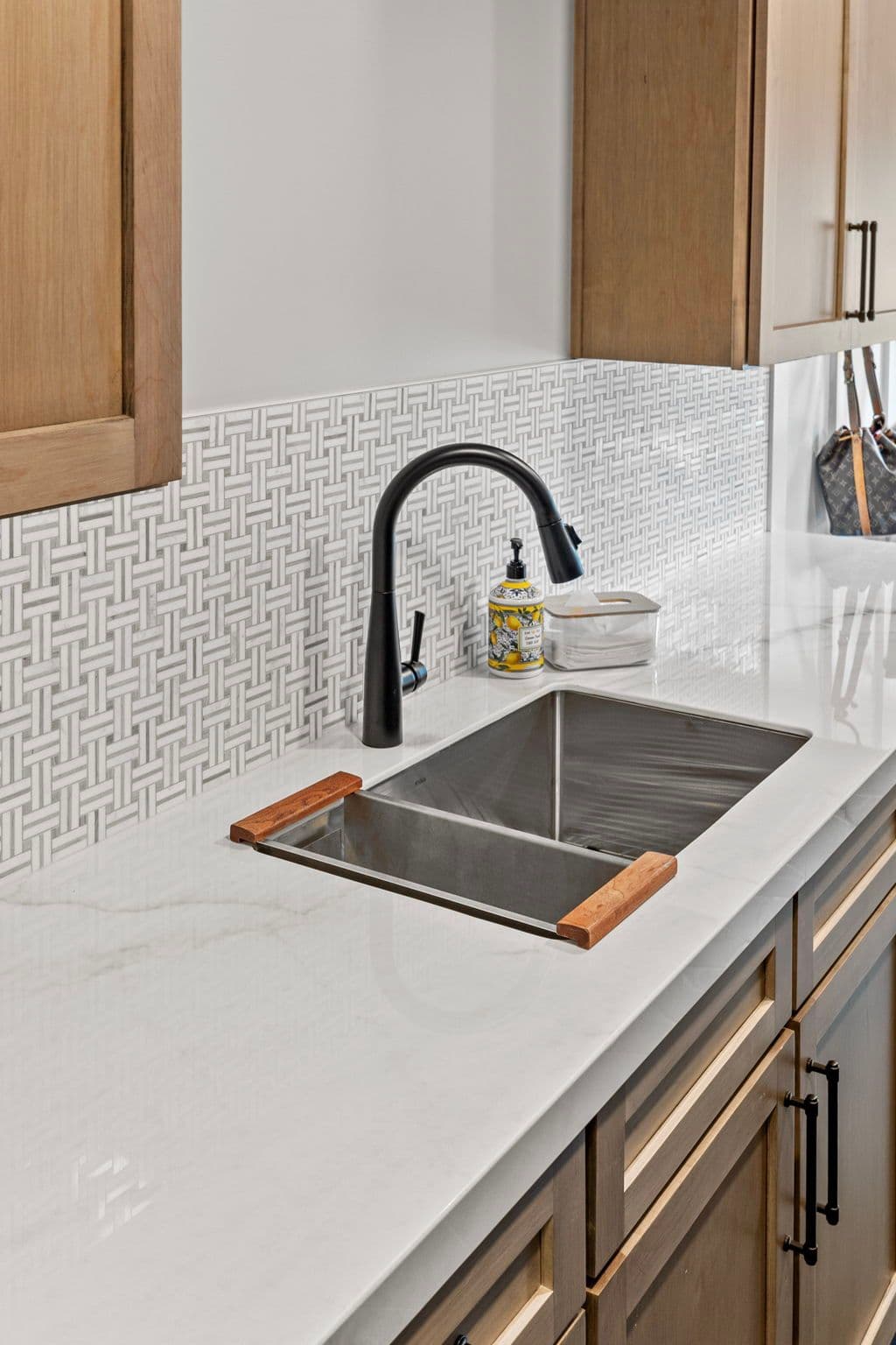 Modern kitchen sink with black faucet, marble countertop, and patterned backsplash.