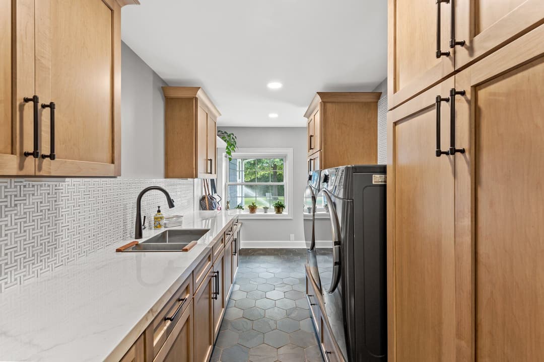 Modern kitchen with wooden cabinets, marble countertop, sink, and laundry area featuring a window.
