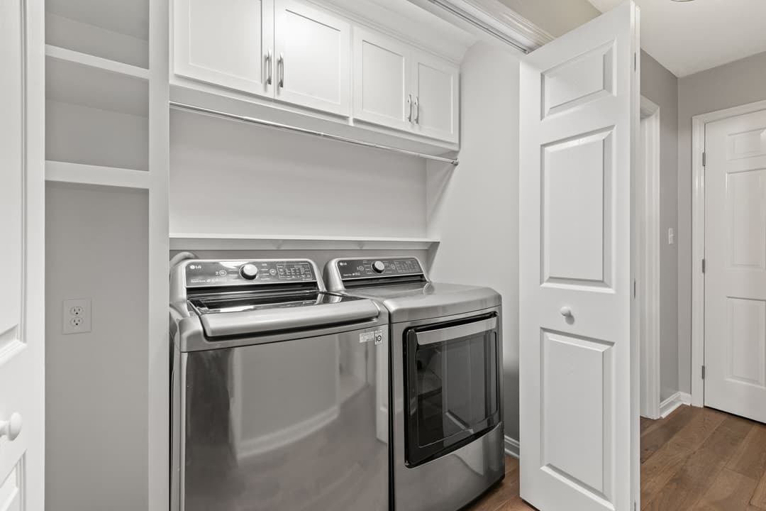 Modern laundry room with stainless steel washer and dryer, white cabinetry, and hardwood floors.