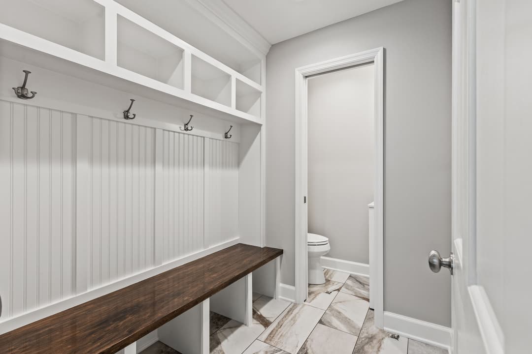 Modern mudroom with white shiplap, wooden bench, and adjacent bathroom door. Spacious and bright.