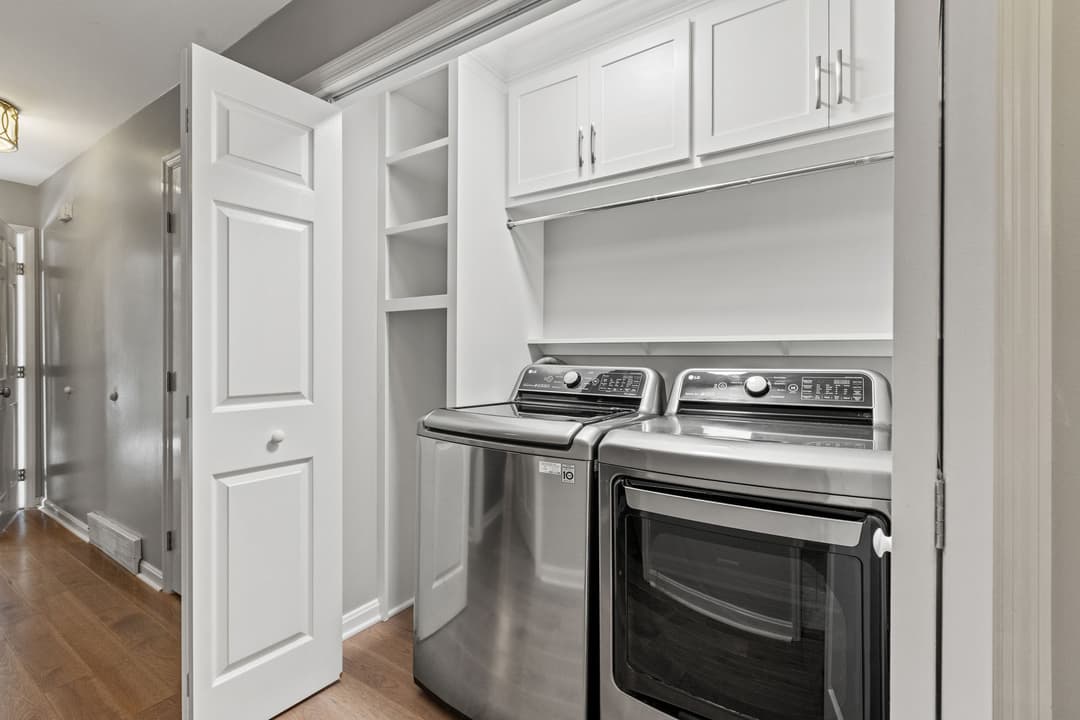 Modern laundry room featuring stainless steel washer and dryer with white cabinetry.