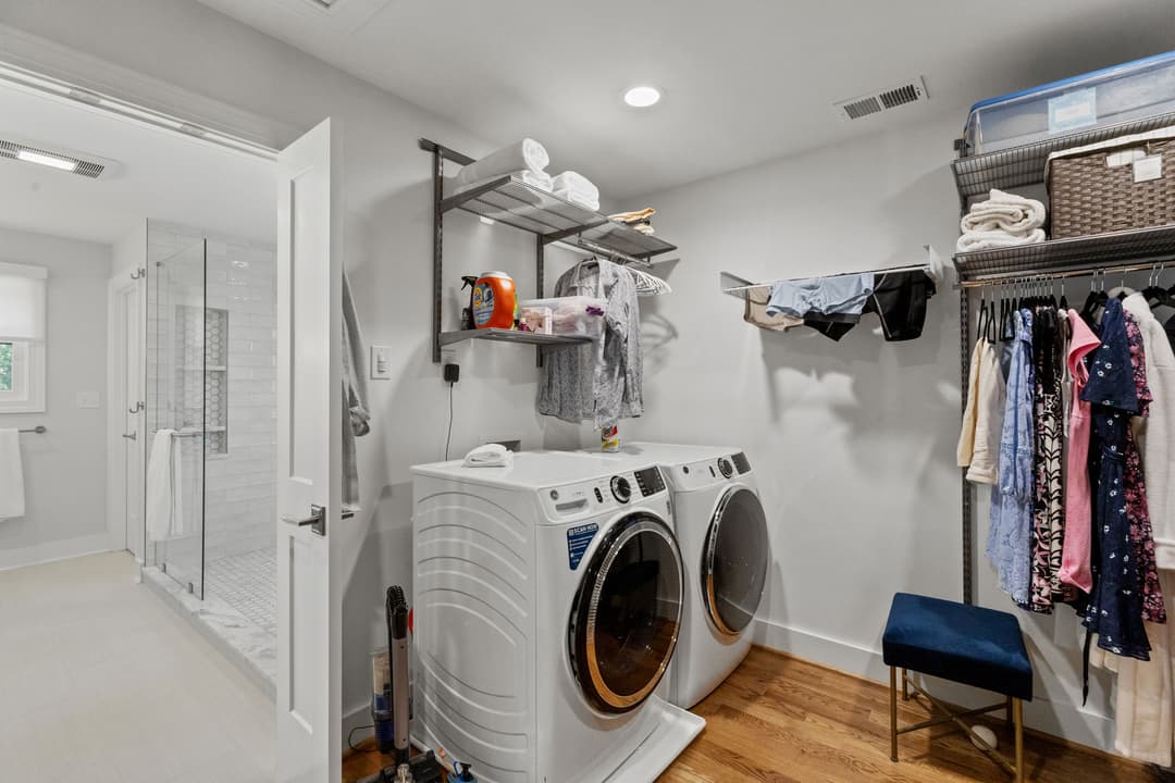 Modern laundry room with stacked washer and dryer, shelving, and hanging clothes. Bright and organized.