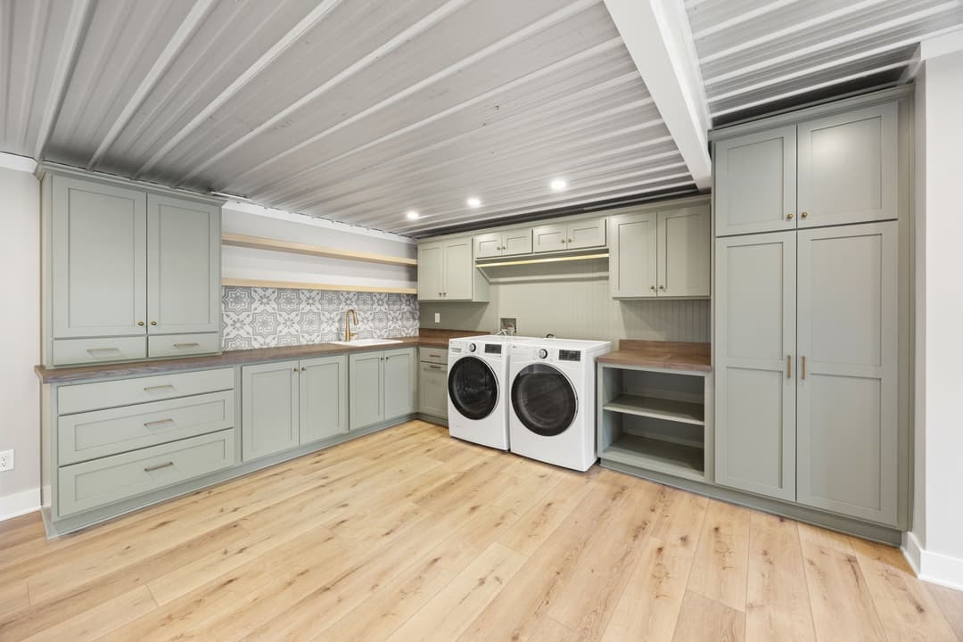 Modern laundry room design featuring gray cabinets, wood countertop, and stacked washer-dryer.