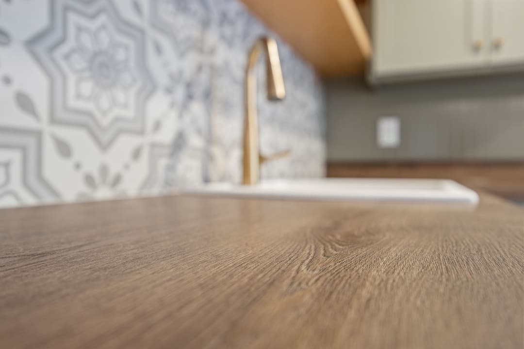 Close-up of wooden countertop with modern sink and decorative patterned backsplash.