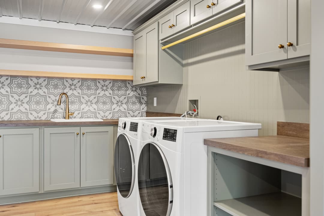 Modern laundry room with white appliances, patterned backsplash, and stylish cabinetry.