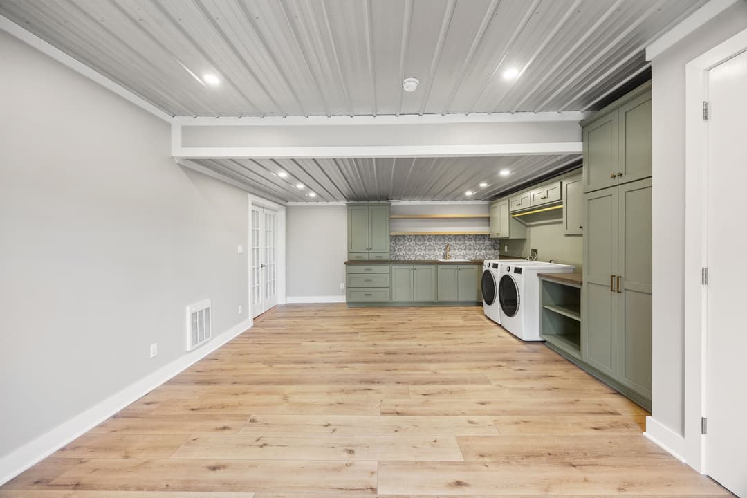 Modern laundry room with green cabinets, wood flooring, and stylish backsplash.