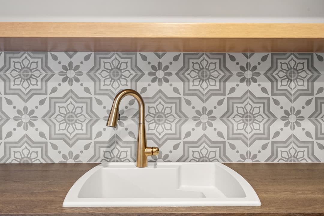 Modern kitchen sink with gold faucet and patterned tile backsplash.