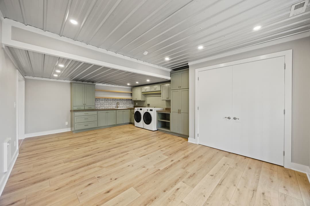 Modern laundry room with light green cabinetry, appliances, and hardwood flooring.
