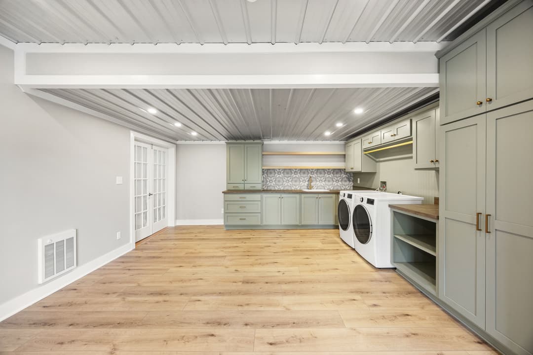 Modern laundry room with mint green cabinets, wood flooring, and stylish backsplash.