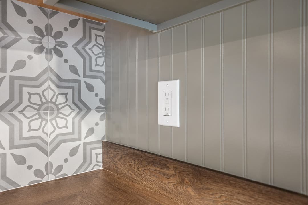 Kitchen backsplash with decorative tiles, wall paneling, and electrical outlet. Modern design.