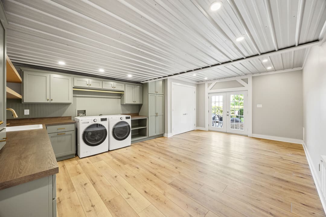 Bright laundry room with modern appliances, wooden flooring, and stylish cabinetry.