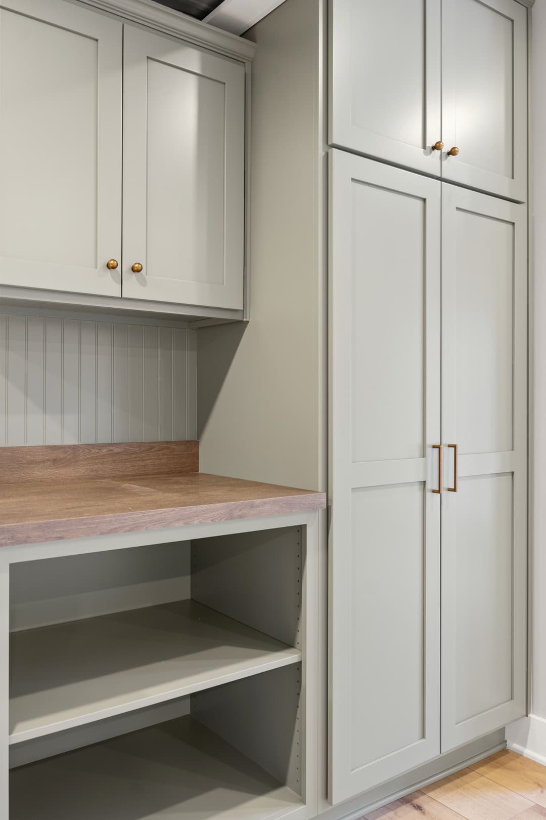 Modern kitchen cabinetry with light gray finish, wooden countertop, and gold hardware.