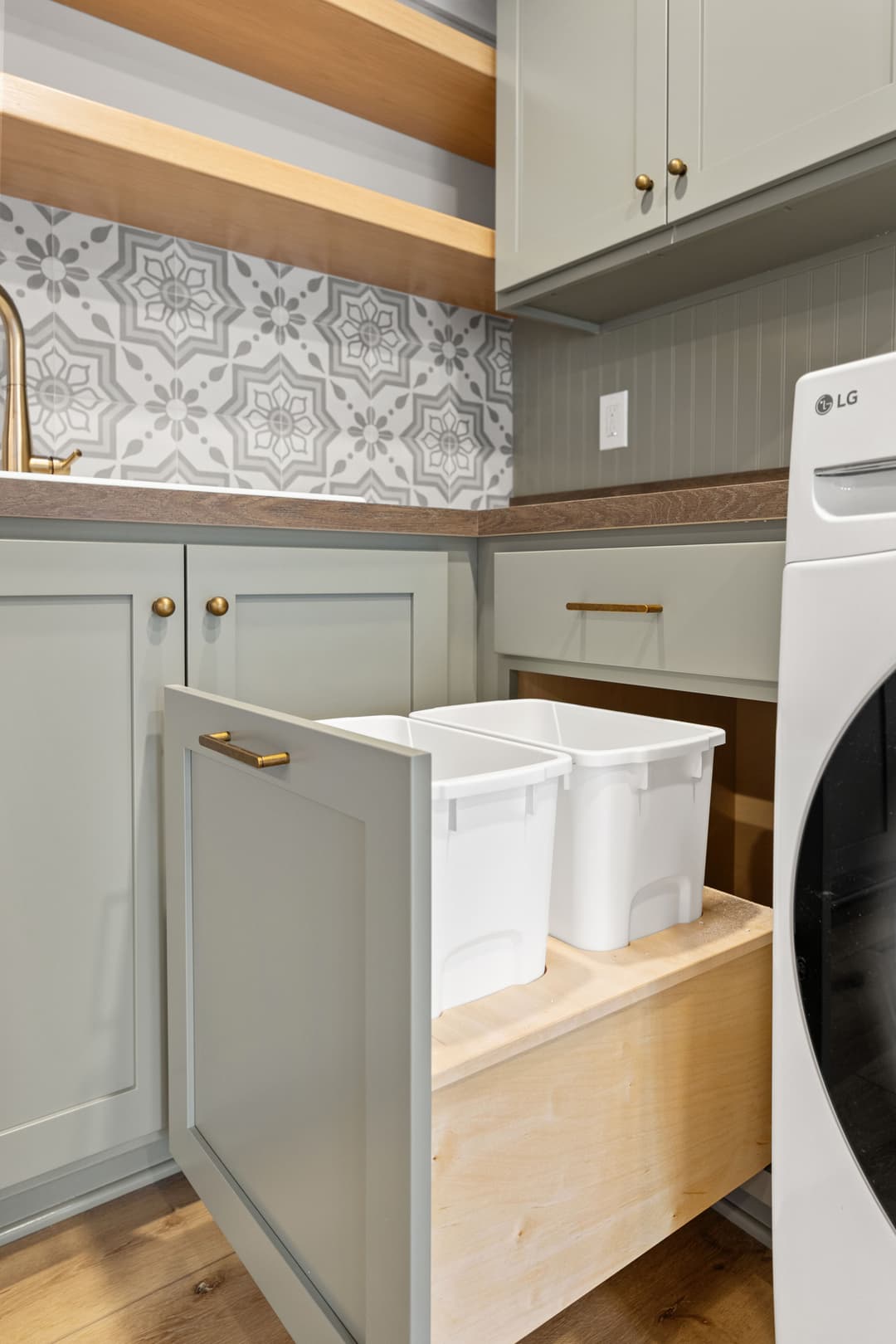 Modern kitchen with a pull-out drawer holding white bins, featuring gray cabinets and patterned backsplash.