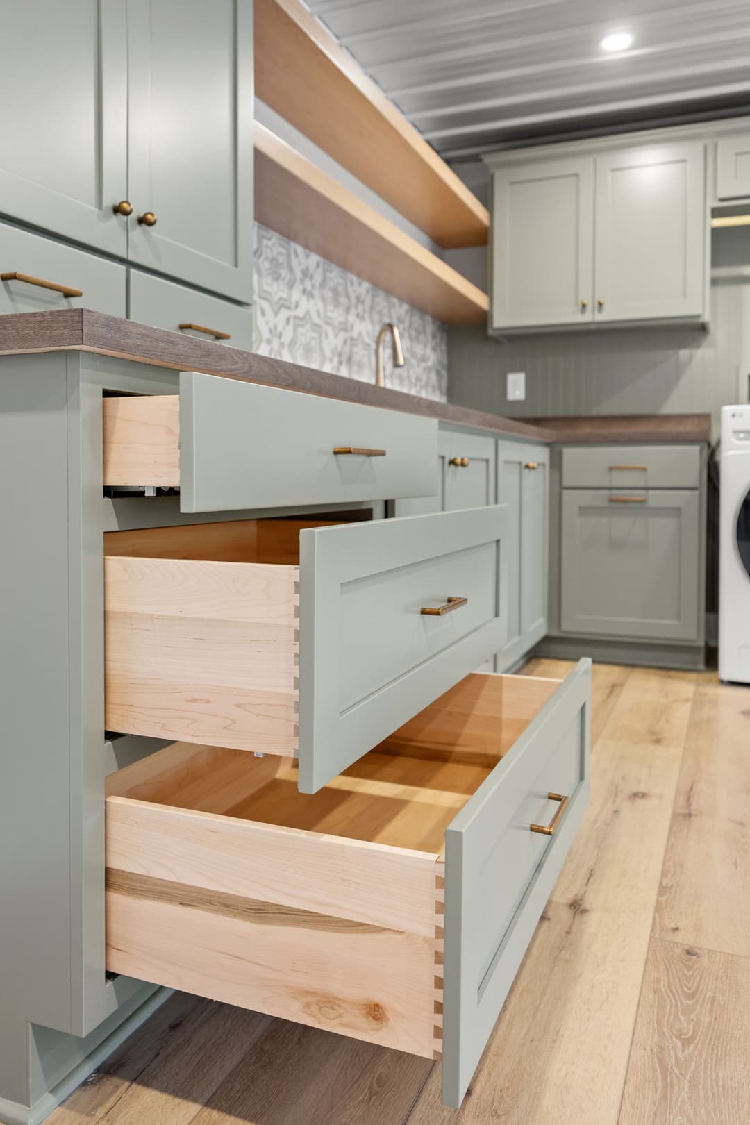 Modern kitchen with light green cabinets and open drawers showcasing wooden interiors.