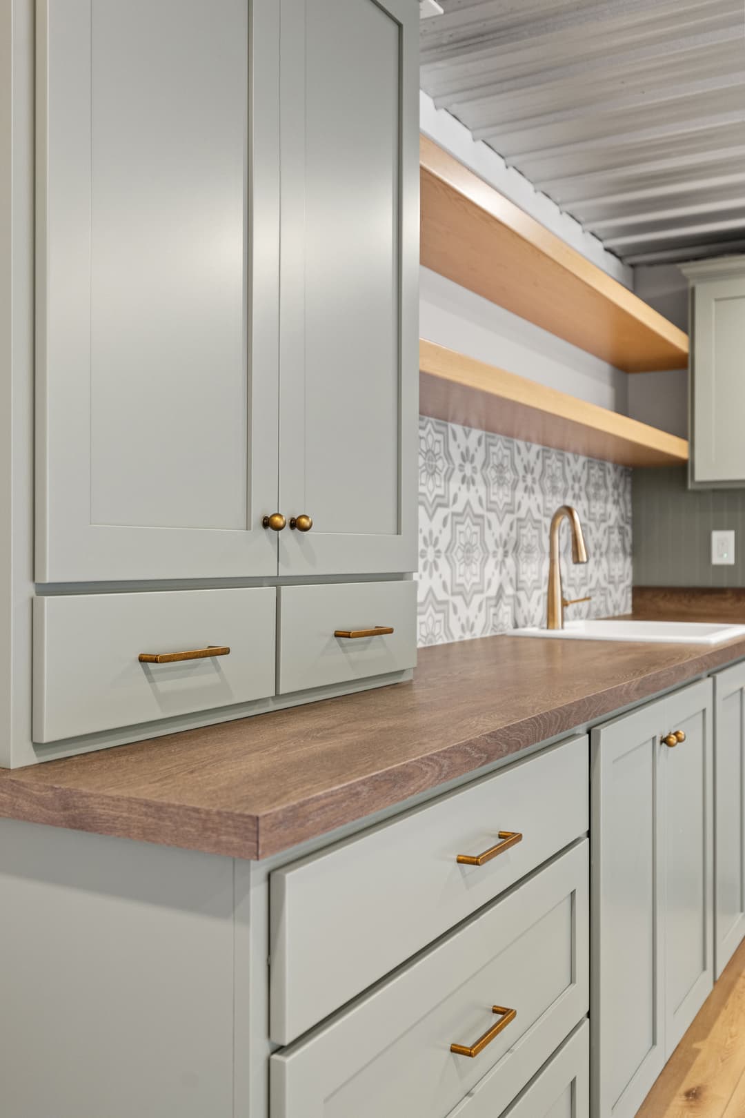 Modern kitchen with light green cabinets, wooden countertop, and stylish patterned backsplash.
